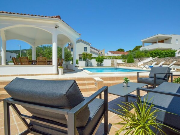 A poolside area with outdoor seating, a covered patio, and a view of the pool and surrounding buildings. - Aquanur by Interhome (Vodice/Tribunj)