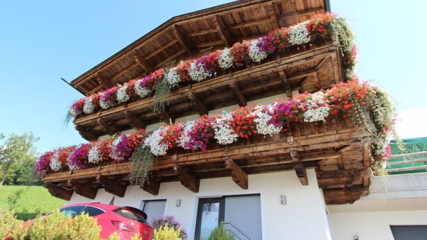 A multi-story building with wooden balconies adorned with colorful flowers. - Wildbachl by Interhome (Aschau im Zillertal)