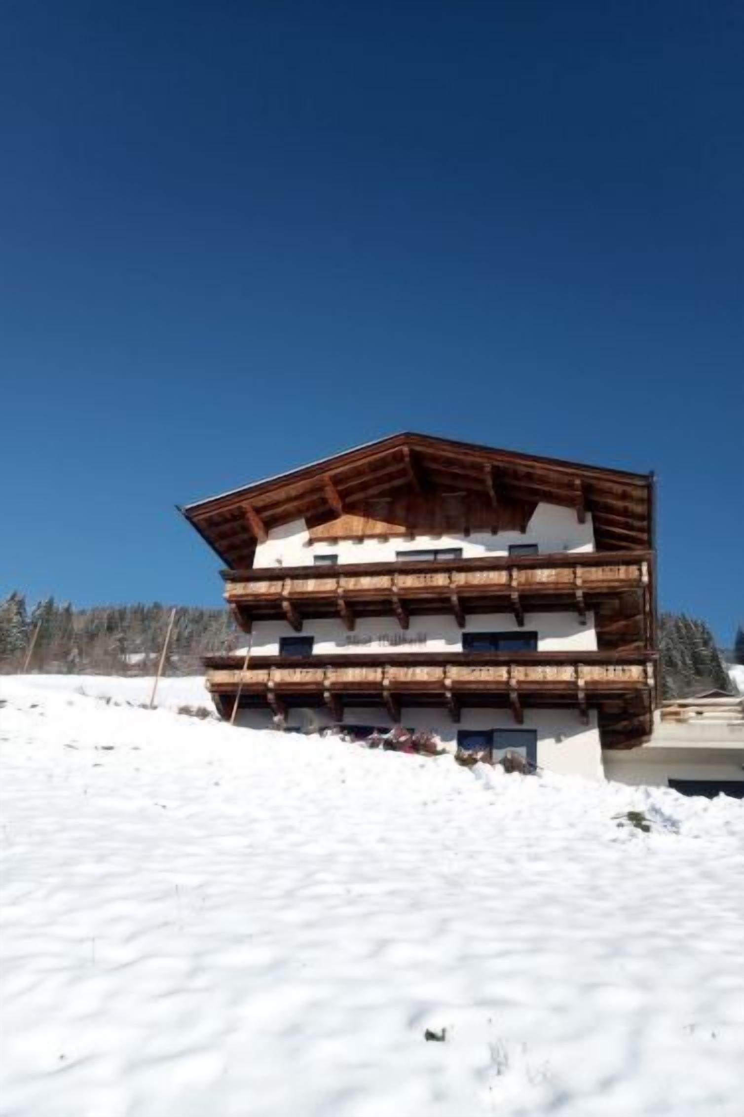 Un chalet en bois à plusieurs étages, doté de balcons, se dressant sur fond de ciel bleu azur.