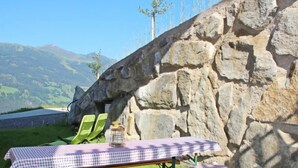 A picnic setup with a checkered table and bench, green chairs, and a stone wall backdrop. - Wildbachl by Interhome (Aschau im Zillertal)