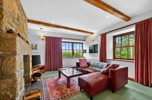 A cozy living room with a stone wall, a fireplace, a leather sofa, a coffee table, and large windows with curtains.