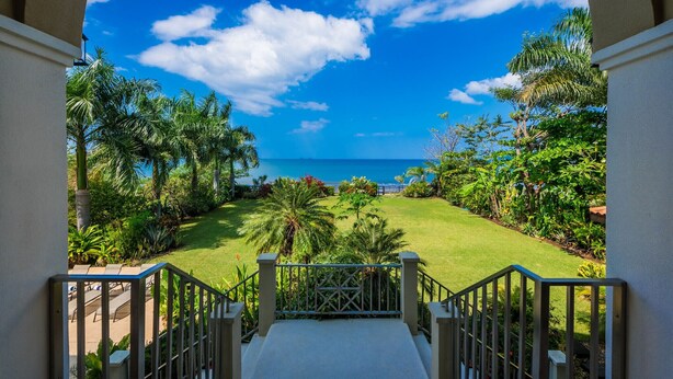 A view from a balcony overlooking a well-maintained garden with palm trees and a clear blue sky. - Potrero Beachfront Villa with Pool & Private Chef - Casa Royal (Potrero)