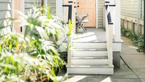 A front porch with steps leading to a door, surrounded by potted plants and a small table with chairs.