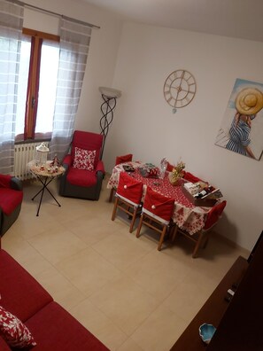 A living room with a dining area, red furniture, a radiator, a clock, and a painting on the wall.