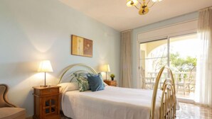 A bedroom with a bed, two bedside tables, a chair, a painting on the wall, and a view of the outdoors through a large window.