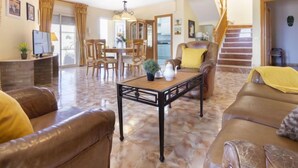 A spacious living room with a brown leather sofa, a coffee table, and a dining area with wooden chairs.