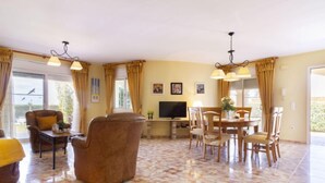 A spacious living room with a large window, a fireplace, and a dining area with wooden furniture.