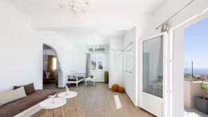 Un salon moderne avec un canapé, deux petites tables, un lustre et une vue sur la ville grâce à de grandes fenêtres.