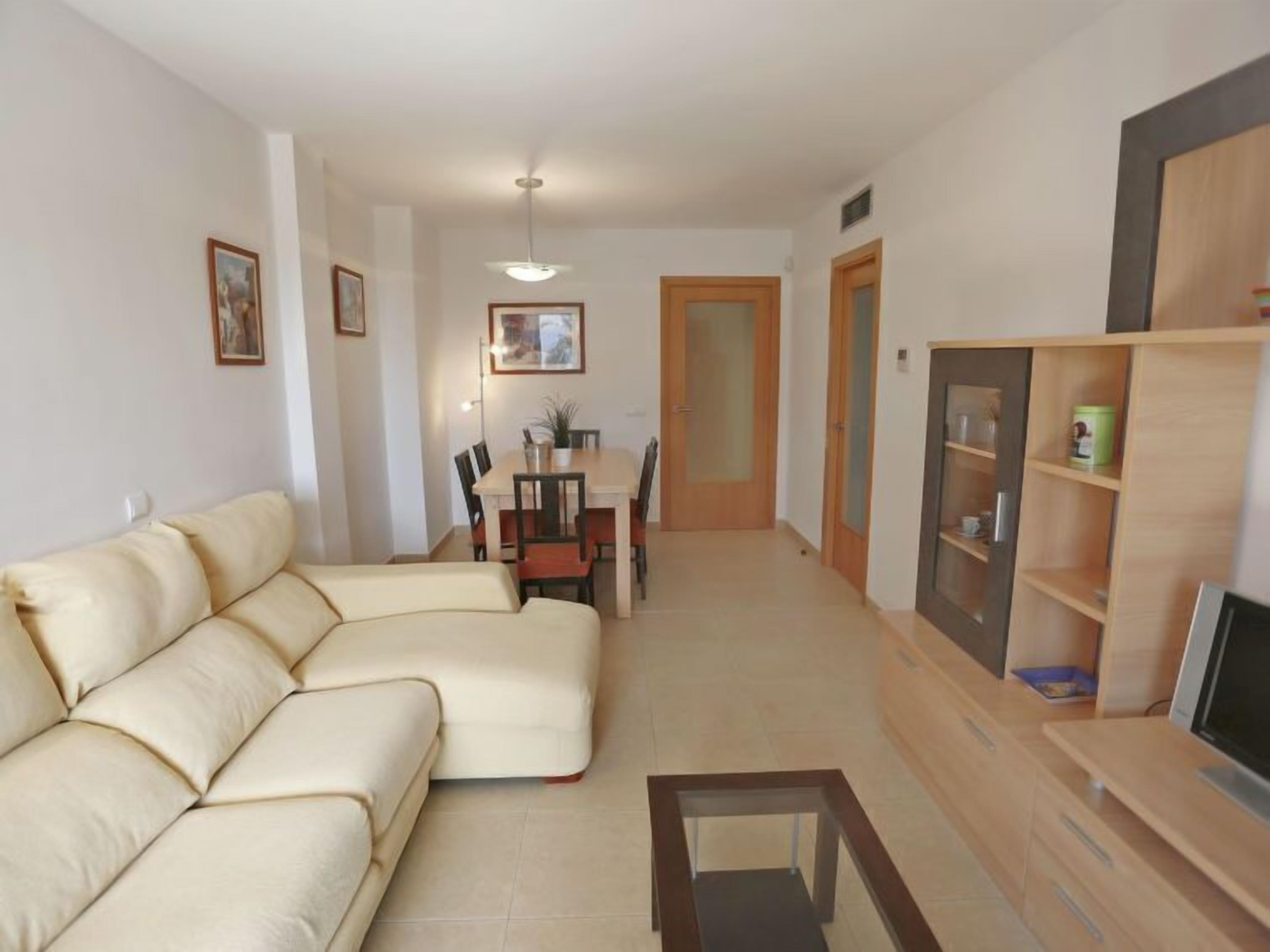 Una sala de estar con un sofá, un mueble para la televisión y un comedor con sillas y una mesa.