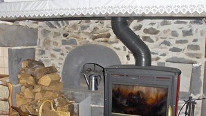 Een houtkachel met schoorsteen, een stenen muur en een metalen waterkoker.