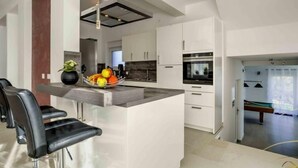 Une cuisine moderne dotée d’un îlot central, de meubles blancs et d’un coin repas avec des tabourets de bar.