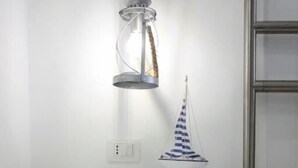 A white bedside table with a drawer and a small shelf, a ship model, and a hanging lantern. - La Pinta overlooking the sea (Tropea)