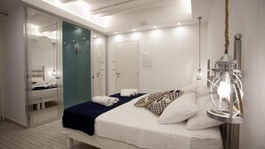 A modern hotel room with a large bed, a glass door leading to a bathroom, and a unique light fixture. - La Pinta overlooking the sea (Tropea)