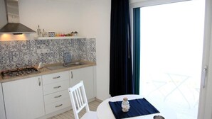 A compact kitchen with white cabinets, a tiled backsplash, a gas stove, and a window with dark curtains. - La Pinta overlooking the sea (Tropea)