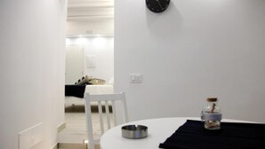 A small, well-lit room with a round table, a chair, a clock on the wall, and a small jar on the table. - La Pinta overlooking the sea (Tropea)