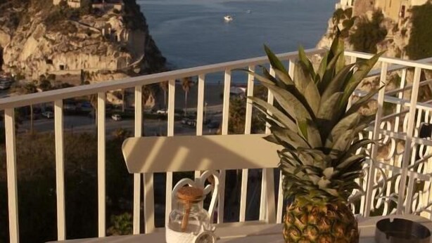 A table with a pineapple, a bowl of fruits, and a bottle on a balcony overlooking a coastal view. - La Pinta overlooking the sea (Tropea)