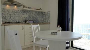 A kitchen with white cabinets, a round table, and a chair. There is a window with curtains and a view of the outside.