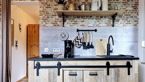 A kitchen with a rustic brick wall, wooden cabinets, a black countertop, and various kitchen utensils. - Eifelhome One nahe Nürburgring by Interhome (Antweiler)