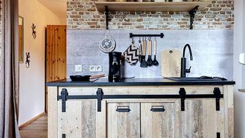 Una cocina con pared de ladrillo rústico, armarios de madera, encimera negra y diversos utensilios de cocina.