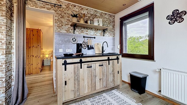 A kitchen with a brick wall, wooden cabinets, a black countertop, and a window with a view. - Eifelhome One nahe Nürburgring by Interhome (Antweiler)