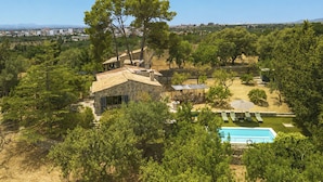 A stone house with a pool, surrounded by trees and a view of a distant city. - Can Coll by Interhome (Selva)