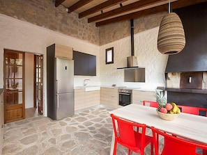 A kitchen with a stone floor, wooden cabinets, a stainless steel refrigerator, a gas stove, and a hanging light fixture.