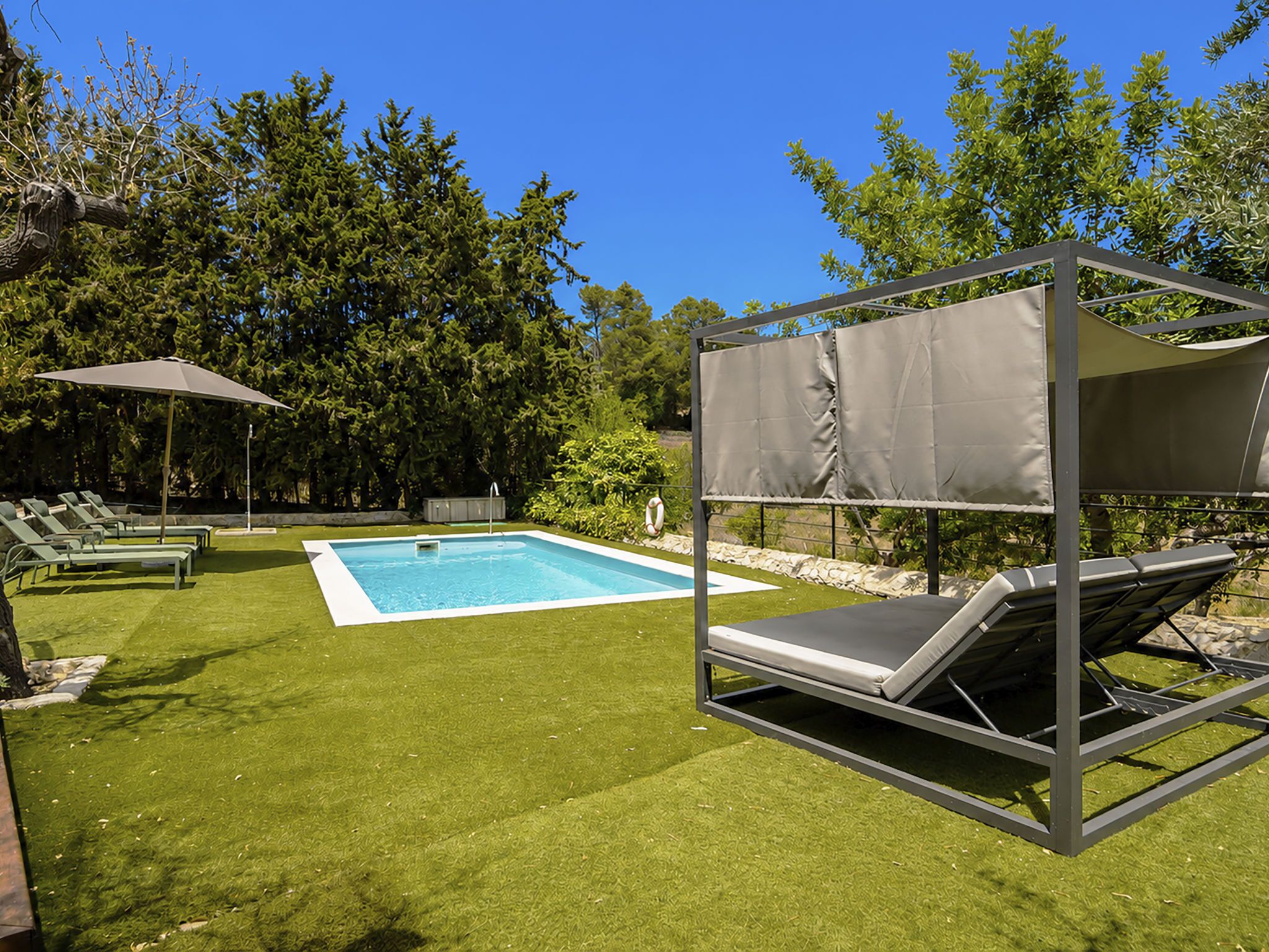 A swimming pool with a shaded area, lounge chairs, and a grassy lawn.