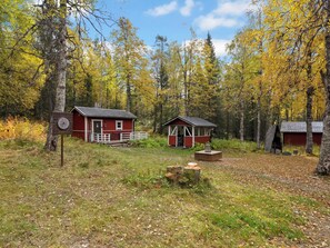 A rustic cabin with a red exterior, surrounded by a forest with autumn foliage.