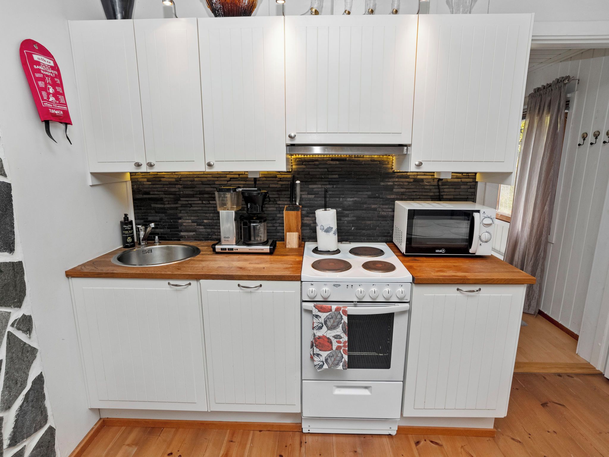 A compact kitchen with white cabinetry, a gas stove, a microwave, and a sink.