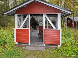 A red wooden cabin with a chimney, a bench, and a door leading to a porch.