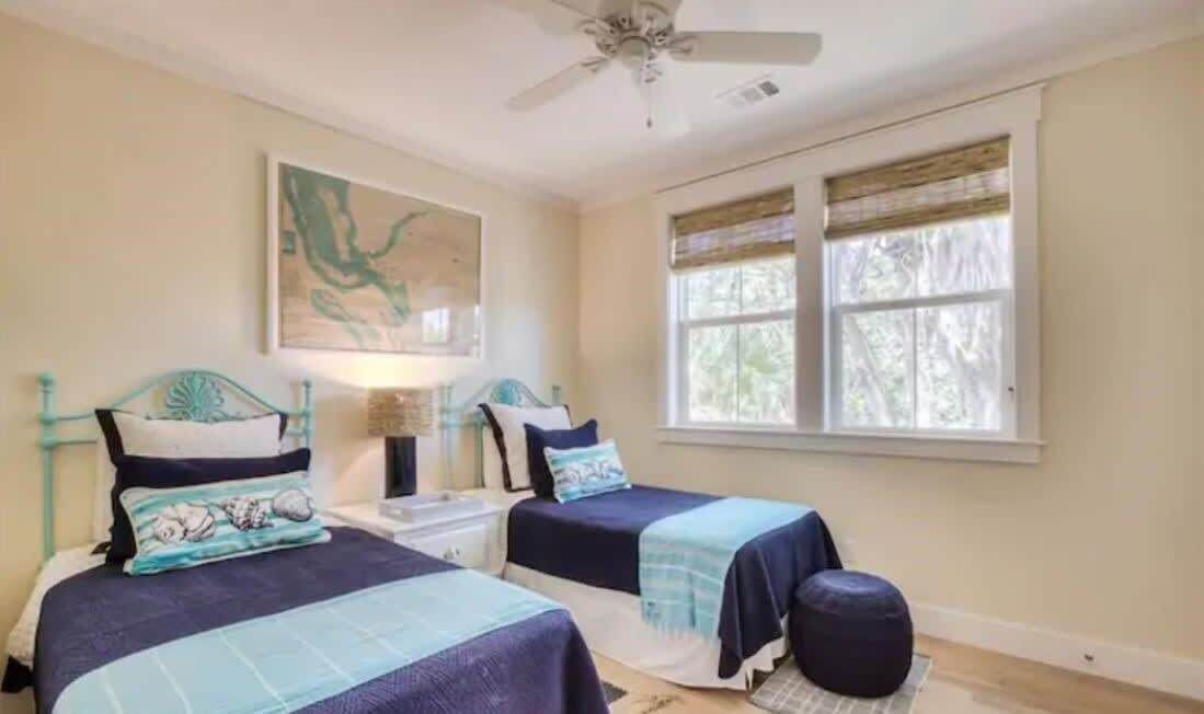 A bedroom with two beds, a ceiling fan, a window with blinds, and a painting on the wall.