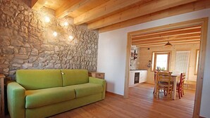 A cozy room with a stone wall, wooden beams, a green sofa, and a dining area with a table and chairs. - Albergo Diffuso - Cjasa Ustin by Interhome (Barcis Lake)