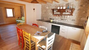 A cozy kitchen with a wooden table, chairs, and a stone wall. - Albergo Diffuso - Cjasa Ustin by Interhome (Barcis Lake)