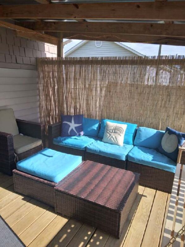 A covered outdoor seating area with a wicker sofa, a chair, and a small table.