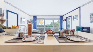 A dining area with a table set for four, a large window with curtains, and a view of greenery outside.