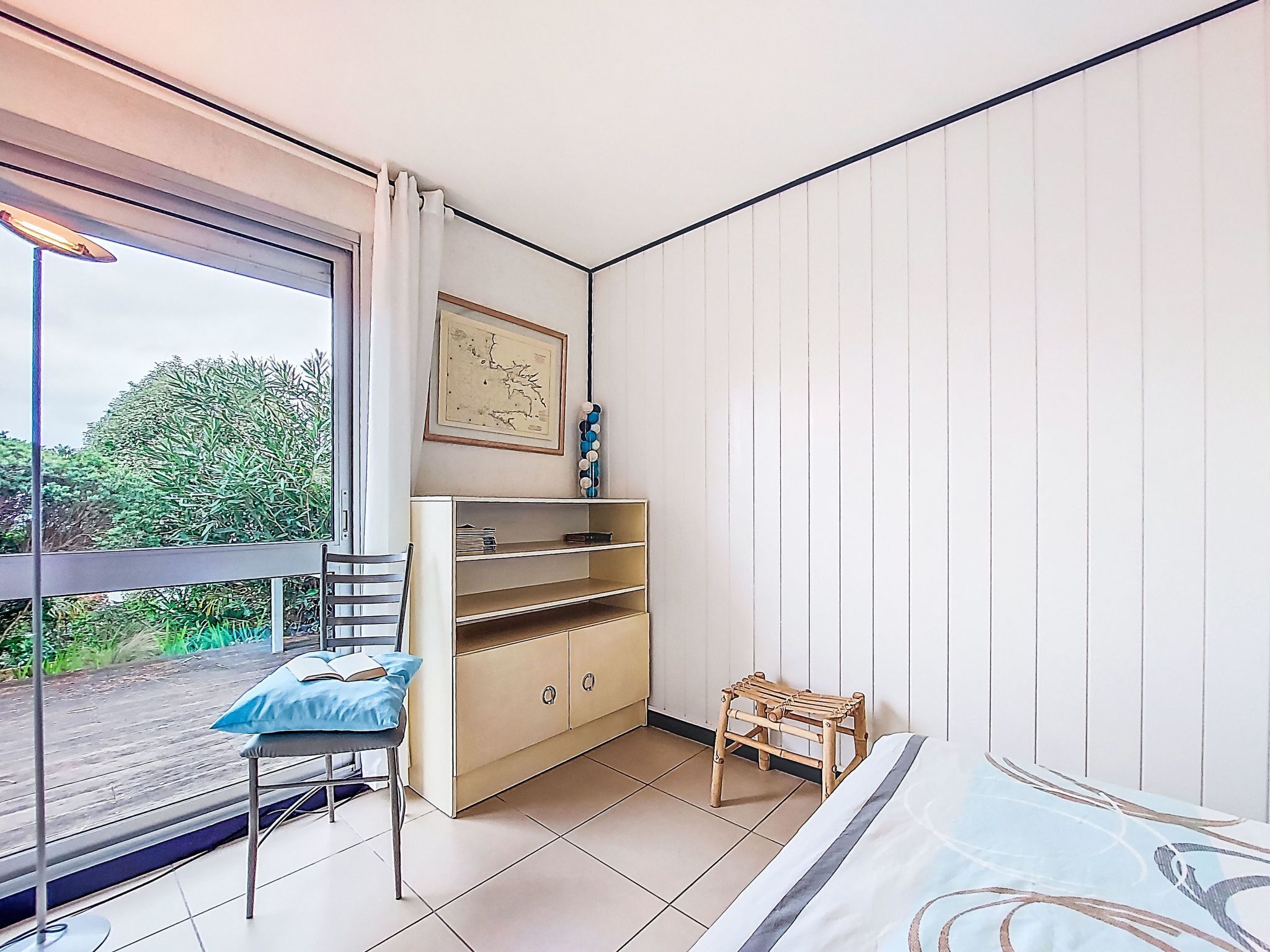 Une pièce comprenant un lit, une petite table avec une chaise, un meuble en bois et une fenêtre donnant sur un paysage verdoyant.