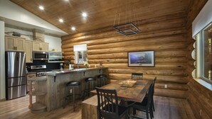 Cocina de estilo cabaña de troncos con paredes de madera, una isla central, taburetes de bar y una mesa de comedor con sillas.