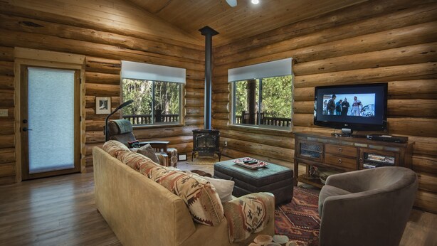 Interior de una cabaña de troncos con un sofá, sillones, un televisor y una chimenea.