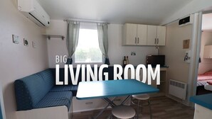 A compact living room with a blue table, a sofa, and a kitchenette area. - Mobile home in seaside private camp 2 (Sukošan)