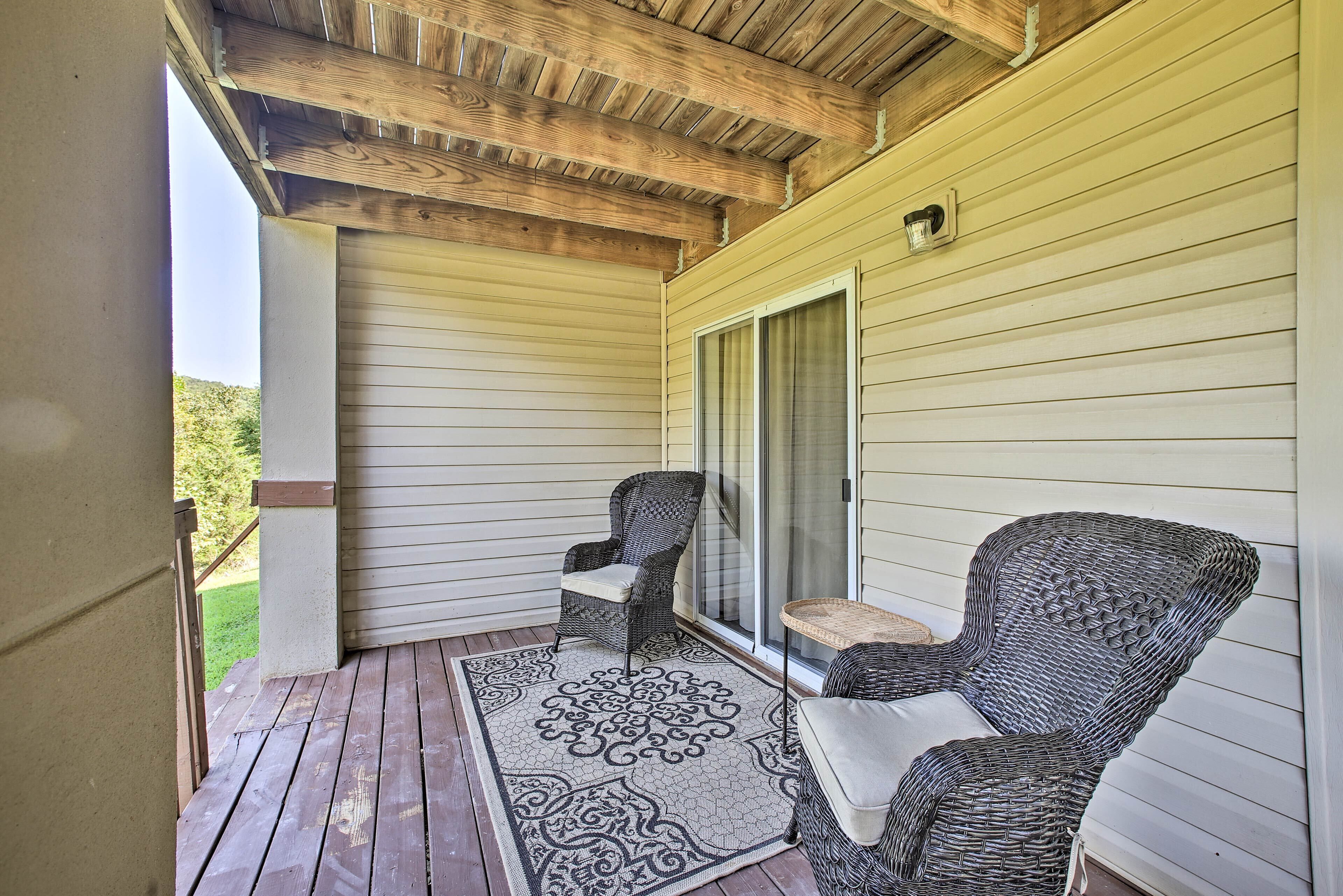 A covered porch with two wicker chairs, a small table, and a patterned rug.