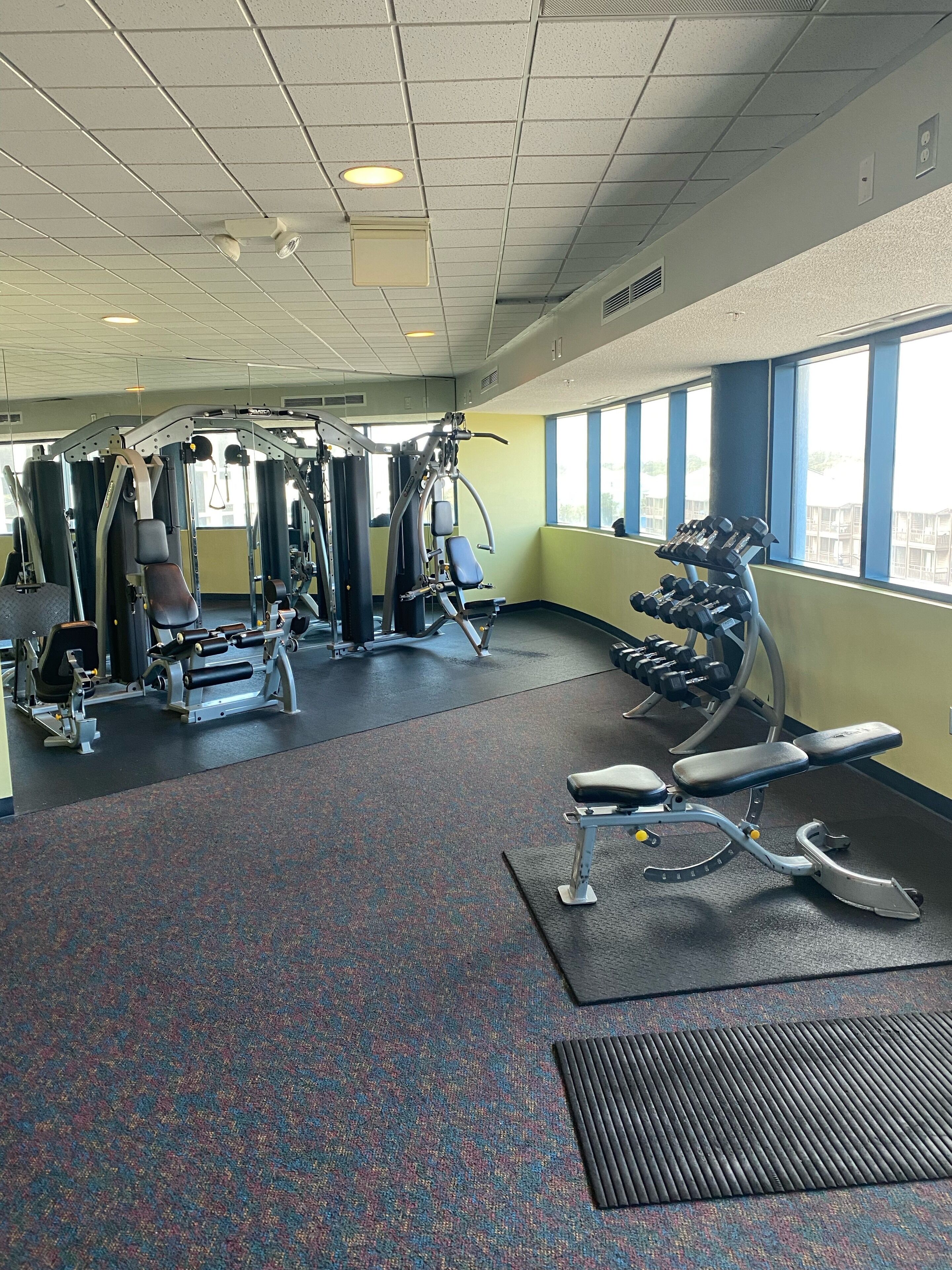 Ein Fitnessstudio mit verschiedenen Trainingsgeräten, einer Bank und Kurzhanteln.