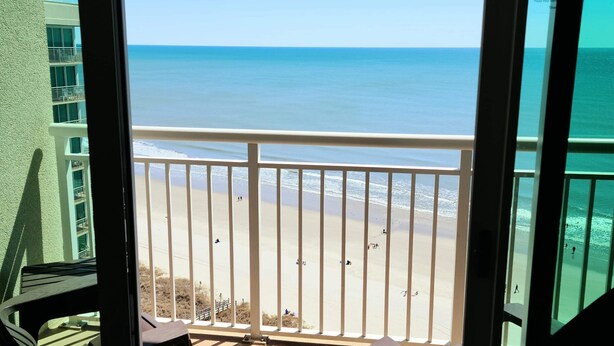 A balcony with a view of the beach and ocean.