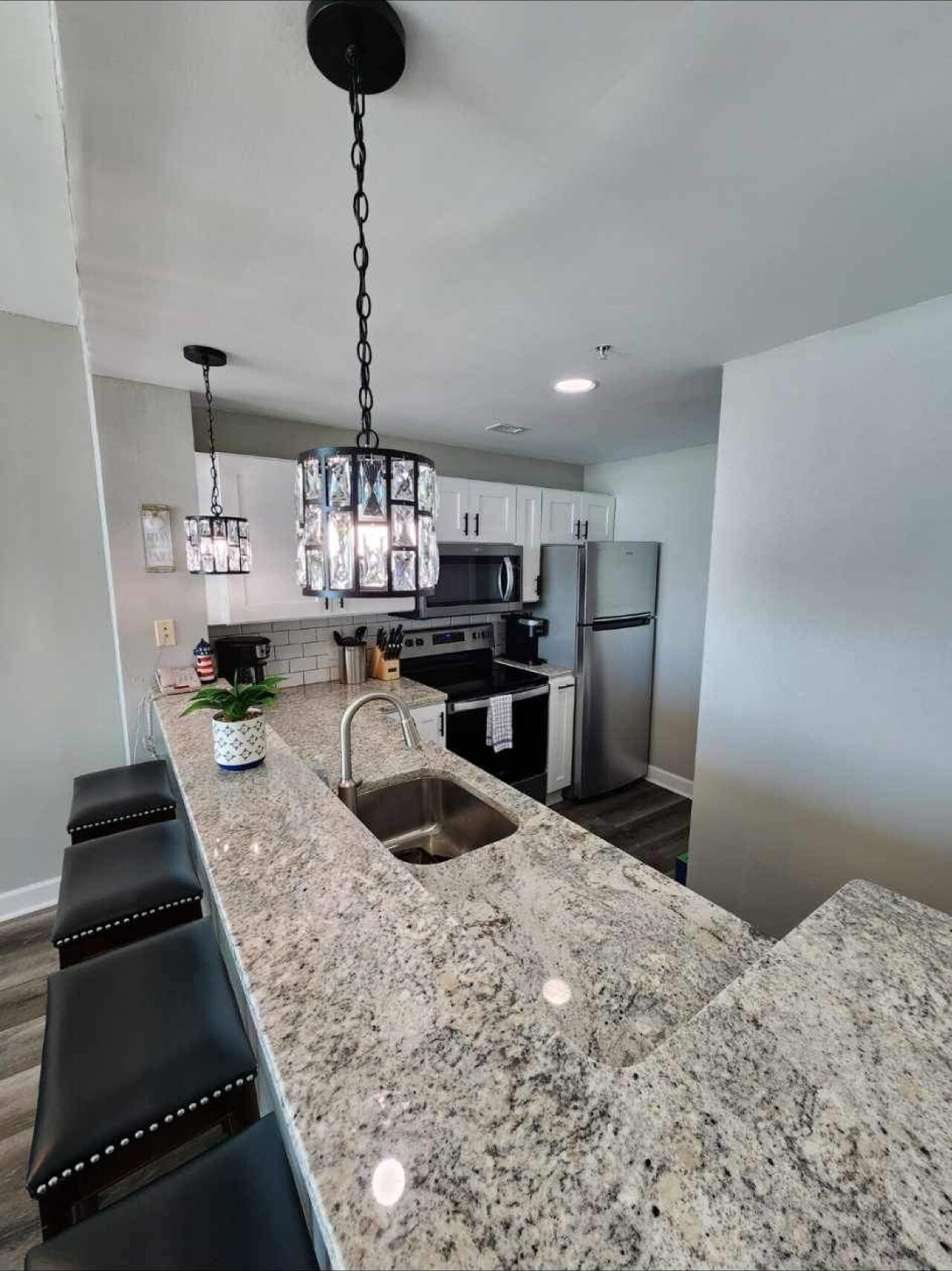 A modern kitchen with granite countertops, stainless steel appliances, and a pendant light.
