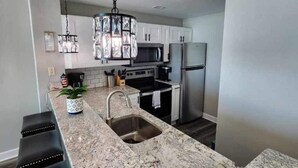 A modern kitchen with granite countertops, stainless steel appliances, and a pendant light.