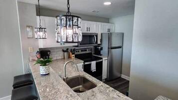 A modern kitchen with granite countertops, stainless steel appliances, and a pendant light.