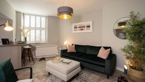 A modern living room with a dark green sofa, a small round table, and a large window with blinds. - Dog friendly apartment with Sky TV by LetMeStay (Ambleside)