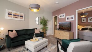 A modern living room with a dark green sofa, a white ottoman, a wooden cabinet, and a television. - Dog friendly apartment with Sky TV by LetMeStay (Ambleside)