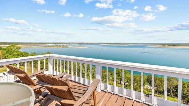 A wooden deck with lounge chairs overlooking a large body of water and distant land.