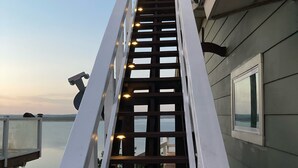 A wooden staircase with white railings leading to a balcony overlooking a body of water.
