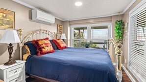 A bedroom with a bed, nightstands, a lamp, an air conditioner, and a window with blinds.